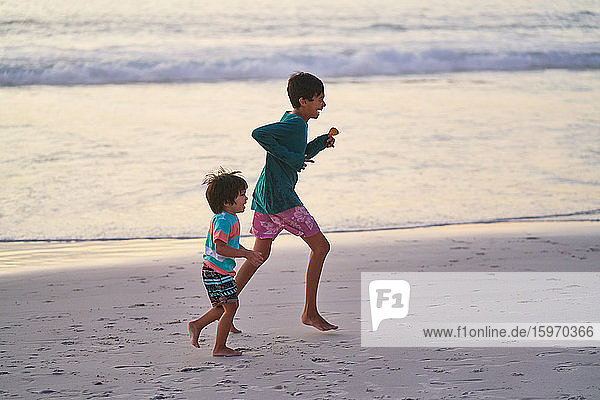 Glückliche Brüder laufen am Strand des Ozeans