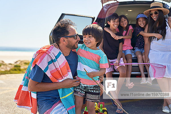 Glückliche Familie vor dem Auto auf einem sonnigen Strandparkplatz