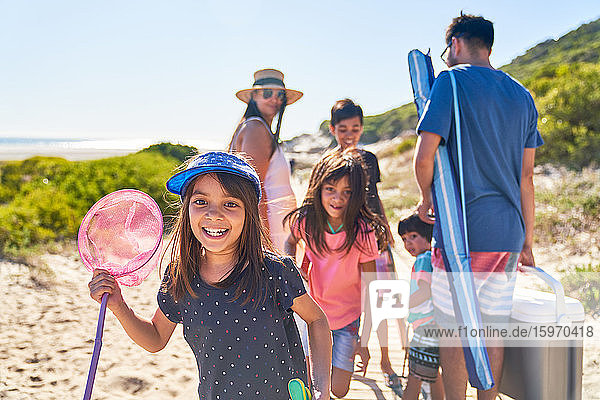 Porträt eines glücklichen Mädchens mit Schmetterlingsnetz am sonnigen Strand mit Familie