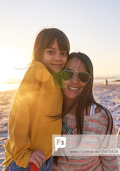 Porträt einer glücklichen Mutter und Tochter am sonnigen Strand bei Sonnenuntergang