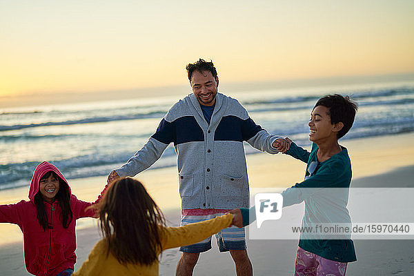 Glücklicher Vater und Kinder halten am Strand bei Sonnenuntergang im Kreis Händchen