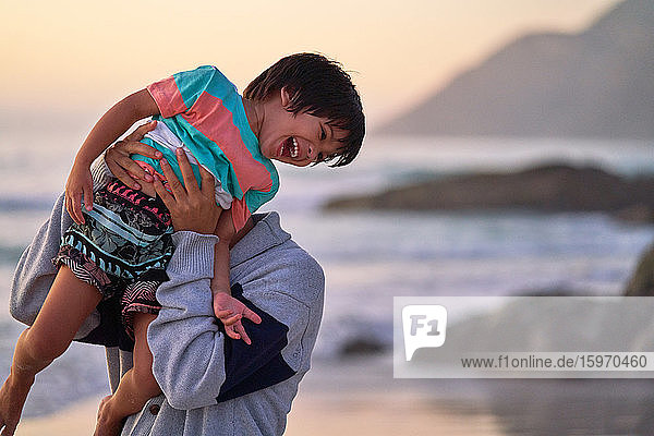 Glücklicher Vater hebt lachenden Sohn am Strand