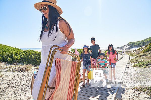 Familie trägt Klappstuhl und Spielzeug auf sonniger Strandpromenade