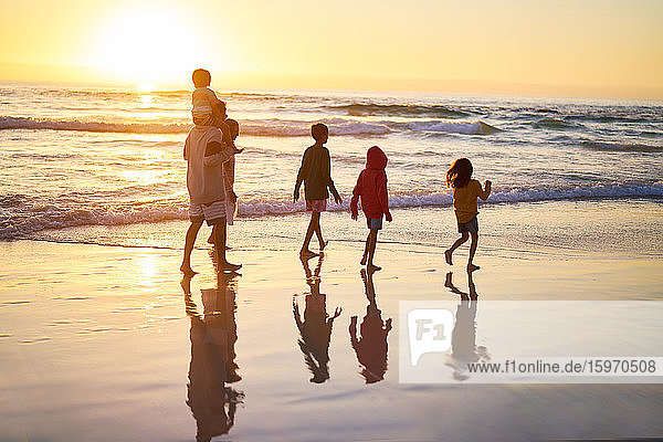 Family walking in ocean surf on beach at sunset
