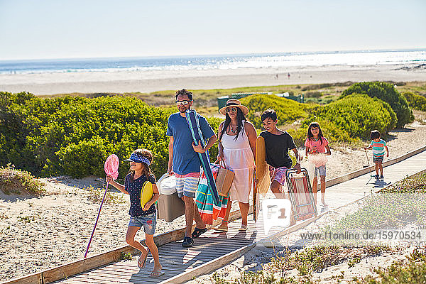 Family carrying chairs and toys on sunny beach boardwalk