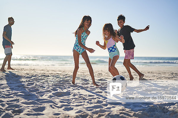 Glückliche Familie spielt Fussball am sonnigen Strand