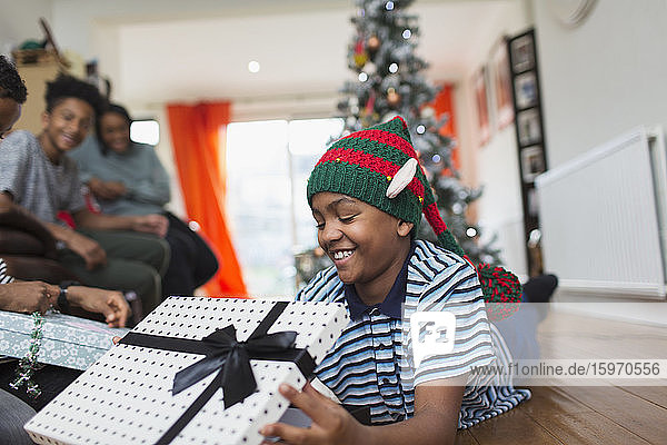 Glücklicher Junge öffnet Weihnachtsgeschenk auf dem Wohnzimmerboden