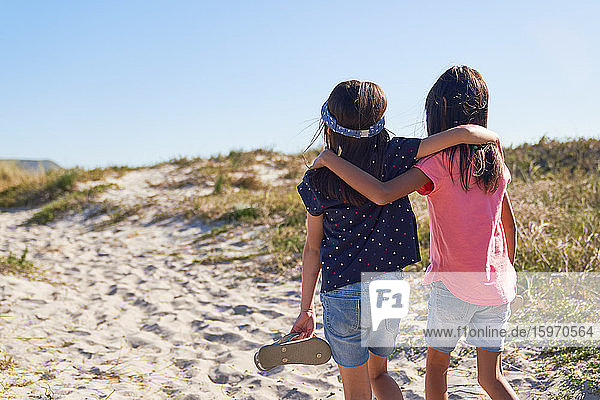 Affectionate sisters walking on sunny beach path
