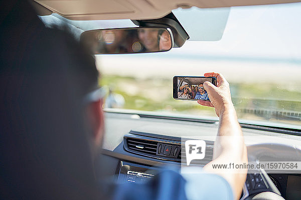 Familie auf Autoreise mit Selfie mit Fotohandy im sonnigen Auto