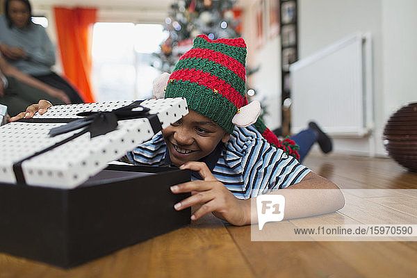 Aufgeregter Junge öffnet Weihnachtsgeschenk auf Wohnzimmerboden