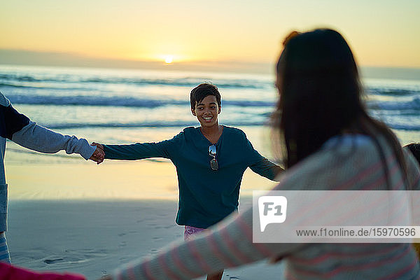 Glückliche Familie hält bei Sonnenuntergang am Strand des Ozeans im Kreis Händchen