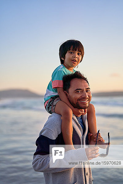 Portrait happy father carrying son on shoulders on beach