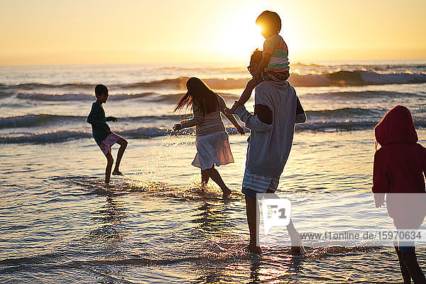 Familie spielt und planscht in der Meeresbrandung bei Sonnenuntergang