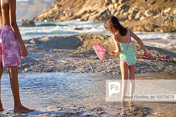 Girl with fishing net playing in tide pool on sunny beach