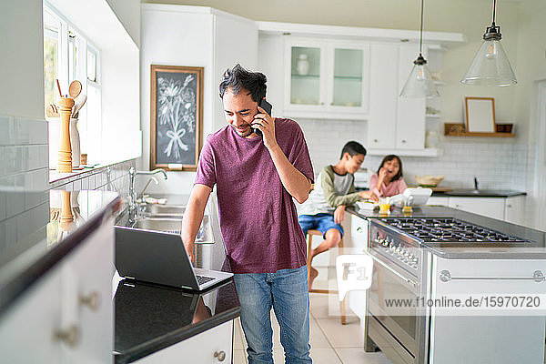Mann arbeitet am Laptop in der Küche mit Kindern beim Essen