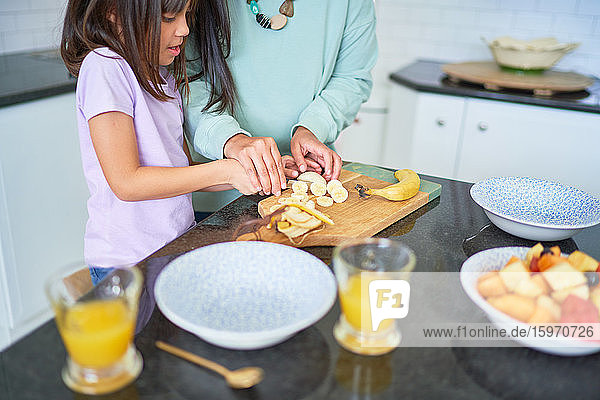 Mutter und Tochter schneiden Bananen in der Küche