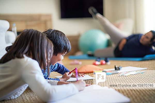 Kids coloring on floor near mom exercising