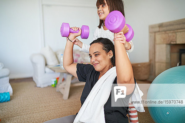 Tochter hilft Mutter beim Training mit Hanteln im Wohnzimmer