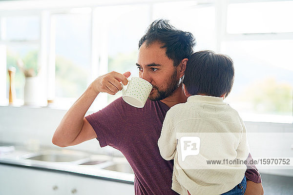 Mann trinkt Kaffee und hält Sohn in der Morgenküche