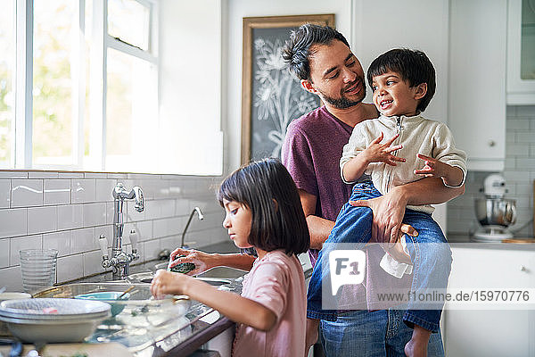 Happy father and kids doing dishes at kitchen sink