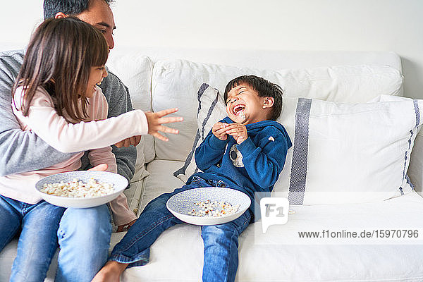 Verspielte Familie mit Popcorn auf dem Wohnzimmersofa