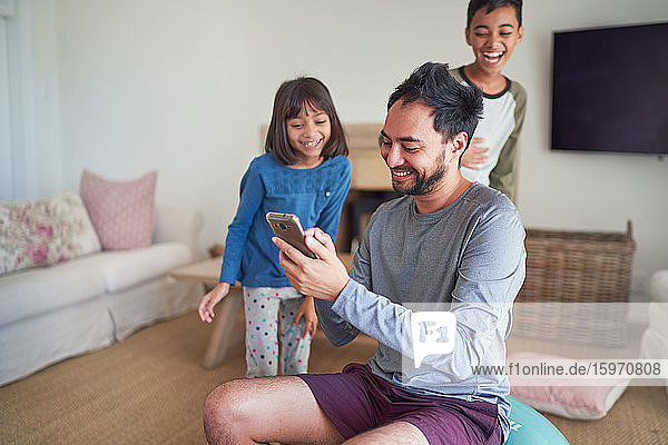 Glücklicher Vater und Kinder mit Smartphone im Wohnzimmer