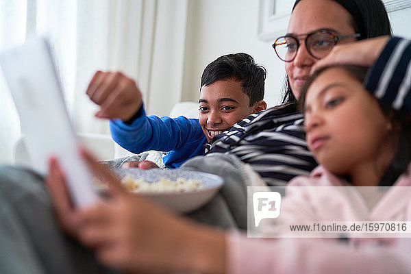 Mutter und Kinder mit Popcorn sehen einen Film auf einem digitalen Tablet