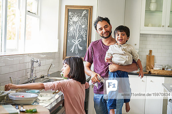 Portrait happy father and kids doing dishes in kitchen