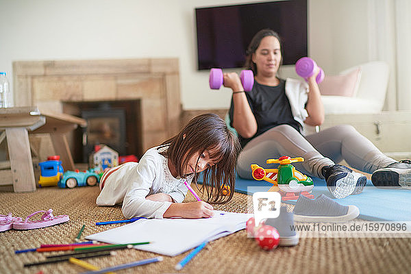 Daughter coloring while mother exercises in living room