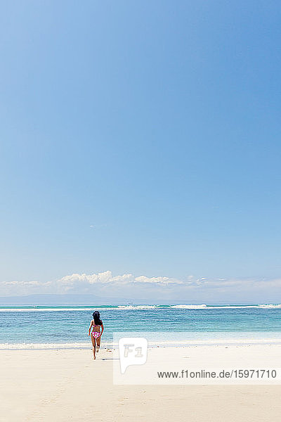 Eine junge Frau läuft an einem unberührten tropischen Strand in den Ozean  Bali  Indonesien  Südostasien  Asien