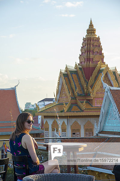 Eine Touristin sitzt in einem Dachrestaurant mit Blick auf einen Tempel in Phnom Penh  Kambodscha  Indochina  Südostasien  Asien