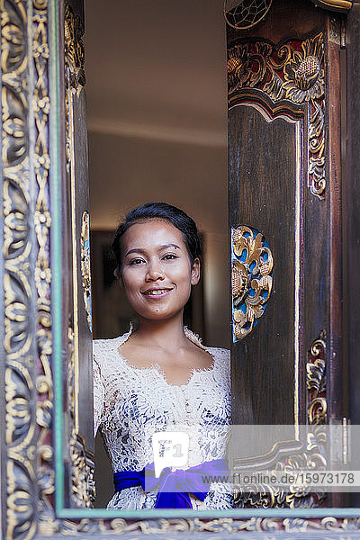 Eine balinesische Frau in traditioneller Kleidung  die aus einem geschnitzten Fenster in einem lokalen Dorf hinaussieht  Bali  Indonesien  Südostasien  Asien