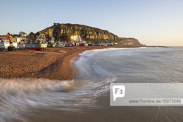 Fishing boats on beach at The Stade with breaking waves and East Hill behind at sunrise  Hastings  East Sussex  England  United Kingdom  Europe