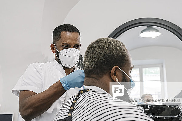 Friseur mit chirurgischer Maske und Handschuhen beim Frisieren eines Kunden