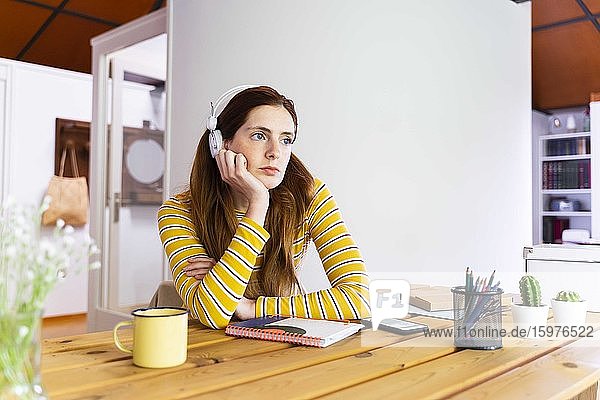 Nachdenkliche junge Frau mit Kopfhörern  während sie am Schreibtisch sitzt
