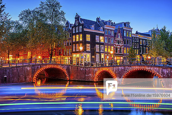 Niederlande  Nordholland  Amsterdam  Lichterketten vor beleuchteter Altstadtbogenbrücke in der Abenddämmerung