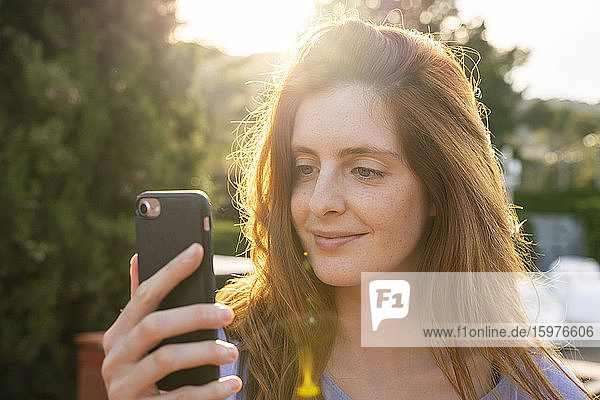 Porträt einer lächelnden rothaarigen Frau  die ihr Smartphone überprüft
