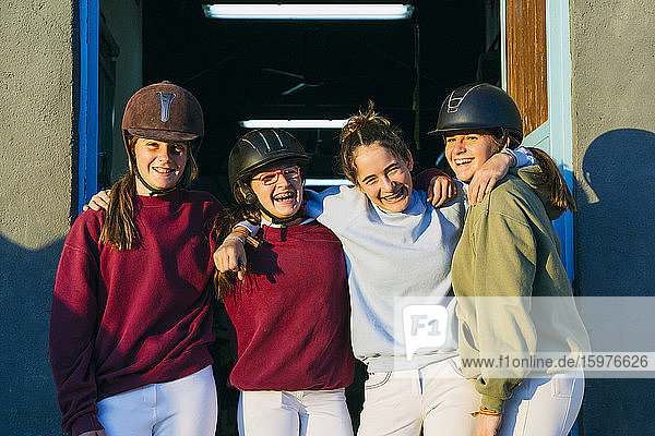 Porträt von fröhlichen weiblichen Jockeys  die an einem sonnigen Tag zusammen vor einem Stall stehen