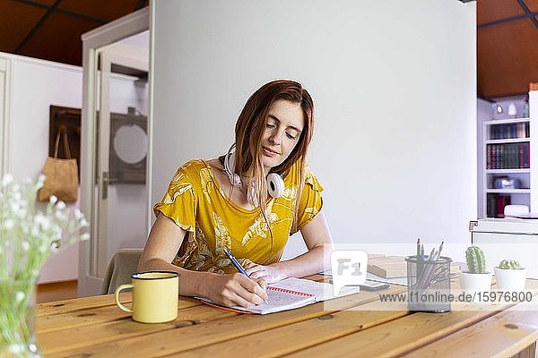 Junge Frau schreibt während der Ausgangssperre in ein Buch und arbeitet zu Hause