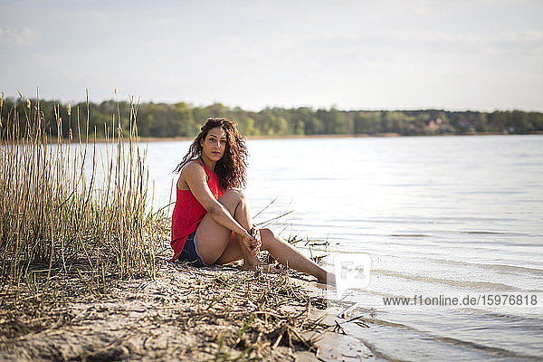 Porträt einer jungen Frau  die am Seeufer sitzt