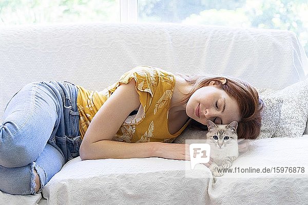 Young woman with closed eyes lying on the couch at home with her cat