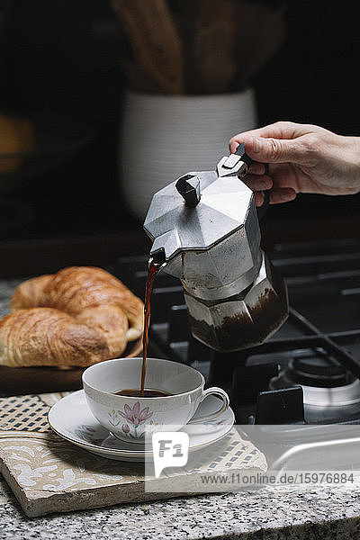 Abgeschnittene Hand einer reifen Frau  die Kaffee in eine Tasse auf dem Küchentisch zu Hause gießt