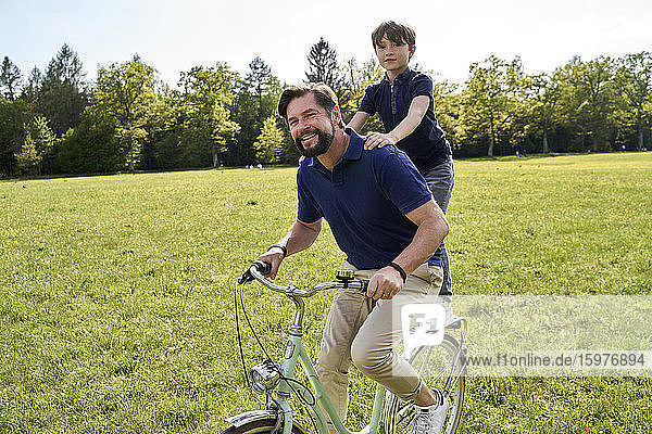 Smiling father and son enjoying bicycle ride on grass during sunny day