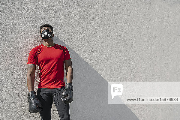 Portrait of a sportsman wearing face mask and boxing gloves at a wall