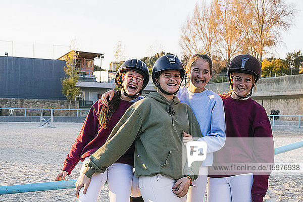 Porträt von fröhlichen weiblichen Jockeys  die auf dem Trainingsplatz gegen den Himmel zusammenstehen