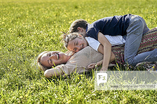 Cheerful woman lying with children on her during sunny day