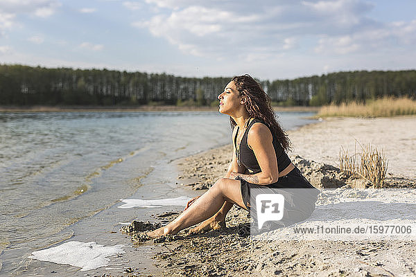 Young woman sitting at lakeshore enjoying sunlight