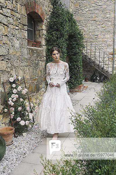 Young woman in elegant wedding dress walking at house
