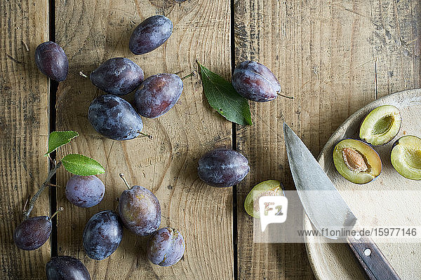 Kitchen knife and fresh plums on wooden surface