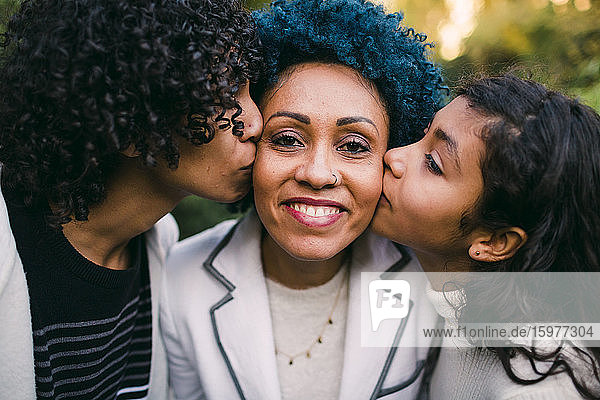 Nahaufnahme von sich liebenden Kindern  die sich im Park auf die Wangen ihrer Mutter küssen